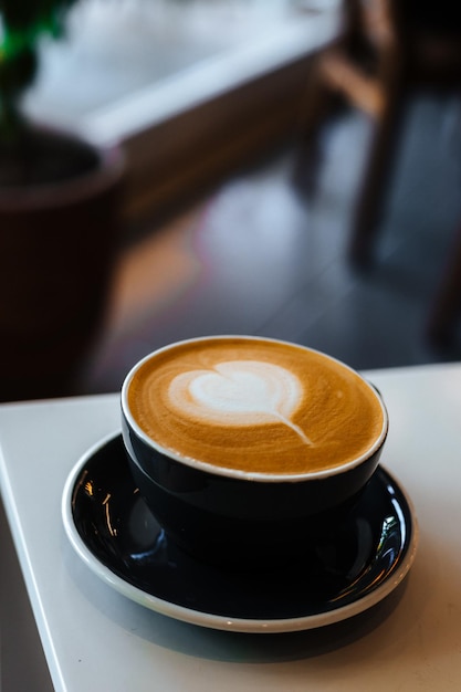 Tazza nera di cappuccino sul piattino con latte art su sfondo bianco da tavola