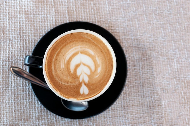 Tazza nera di latte d'arte su un caffè cappuccino su sfondo beige vista dall'alto in un caffè Fiore di schiuma