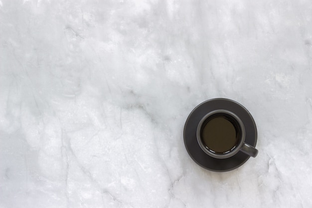 Tazza nera sul piattino con caffè nero sul fondo della tavola di marmo.