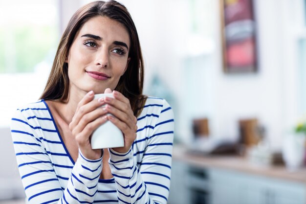 Tazza premurosa della tenuta della giovane donna a casa