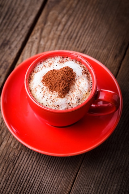 Tazza rossa con cappuccino e decorazione a cuore su schiuma. Coppa di San Valentino. concetto di amore