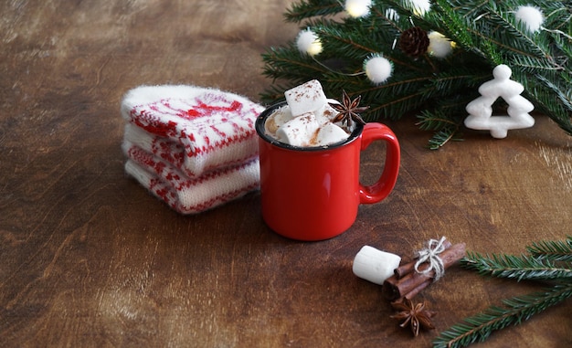 Tazza rossa con cioccolata calda con marshmallow e guanti e rami di albero di natale sul tavolo di legno. Copia spazio