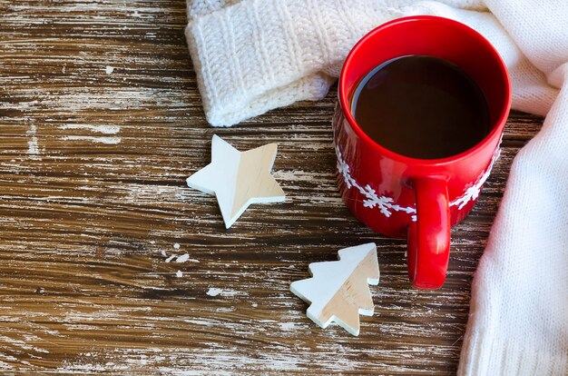 Tazza rossa di caffè e maglione lavorato a maglia bianco accogliente sul retro. Deliziosa bevanda per il freddo. Orari invernali o concetto di mattina di Natale.