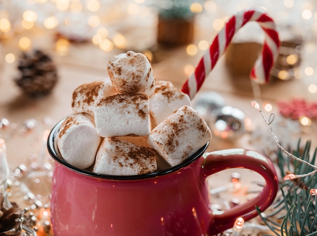 Tazza rossa di cioccolata calda con bastoncino di zucchero su sfondo di legno di Natale con luci di Natale bokeh, atmosfera di Natale e Capodanno