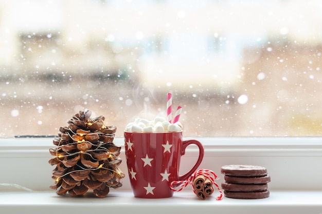 Tazza rossa di cioccolata calda o bevanda al cioccolato con marshmallow sul davanzale della finestra