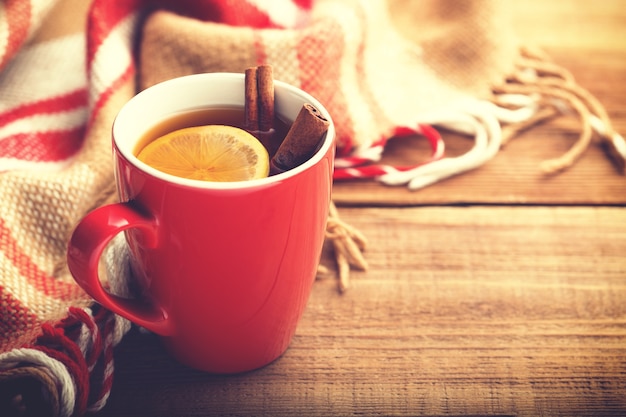 Tazza rossa di tè caldo con limone e cannella.