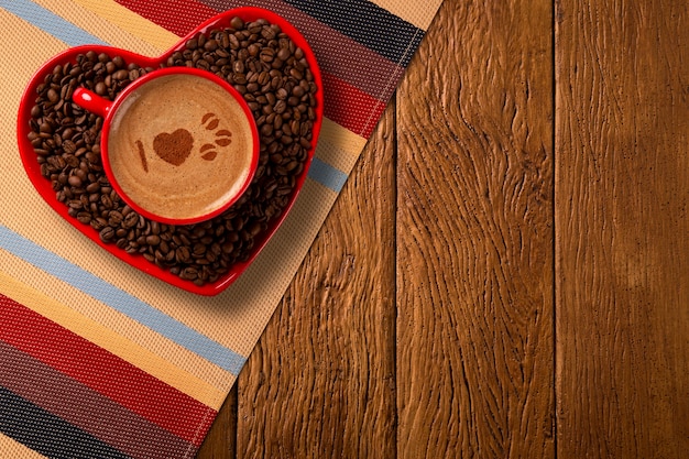 Tazza rossa e piattino da caffè a forma di cuore con caffè decorato su fondo di legno vecchio. Vista dall'alto. Scritto in inglese amo la forma del caffè nel caffè.