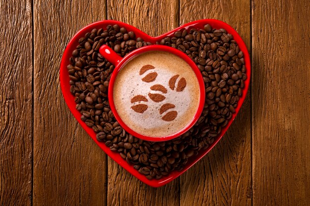 Tazza rossa e piattino da caffè a forma di cuore con caffè decorato sul vecchio spazio di legno. Vista dall'alto. forma del chicco nel caffè.