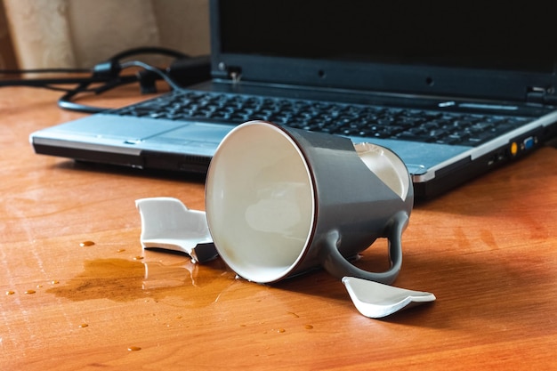Tazza rotta e tè o caffè versati vicino al laptop in ufficio