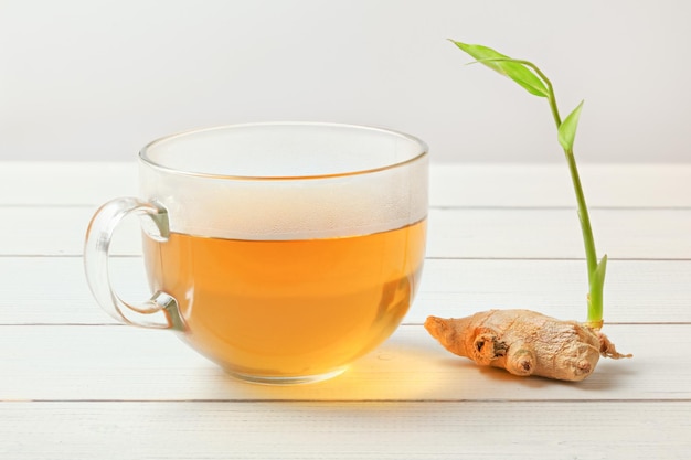 Tazza trasparente con tè caldo, bagnato dal vapore su vetro, radice di zenzero secca con germoglio verde accanto.