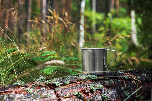 Tazza turistica in metallo con bevanda calda si erge sul tronco d'albero nella foresta