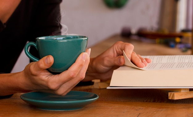 Tazza verde con caffè caldo nelle mani della donna con libro di lettura a casa concentrarsi sulla tazza