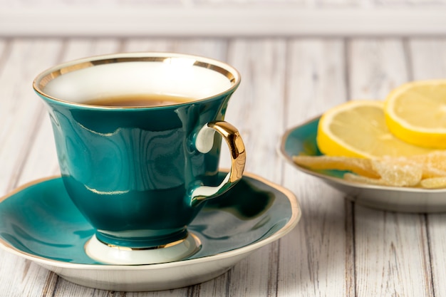 Tazza verde di tè caldo e piattino con limoni e zenzero candito su un tavolo di legno. Avvicinamento