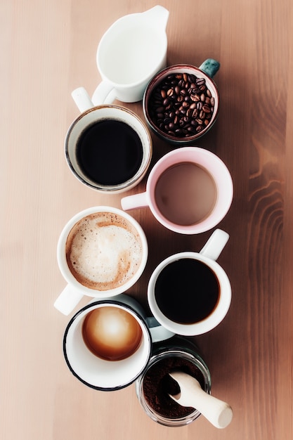 Tazze da caffè multiple e tazze multicolori con americano, espresso, latte e cappuccino, barattolo di latte, chicchi di caffè tostato in bottiglia di vetro, cucchiaio di legno e caffè macinato in barattolo su fondo di legno