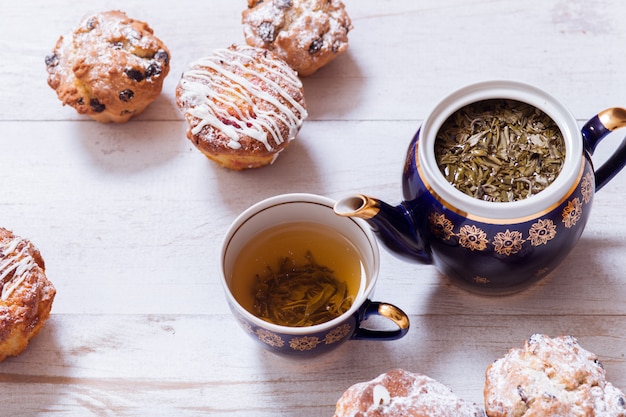 Tazze da tè, teiera e muffin sulla tavola di legno bianca