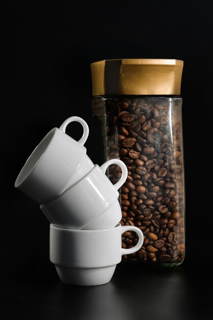 Tazze di caffè bianche e un barattolo di caffè su sfondo nero