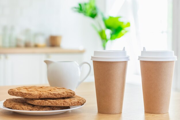 Tazze di caffè da asporto e biscotti di zucchero in cucina con la luce del sole.