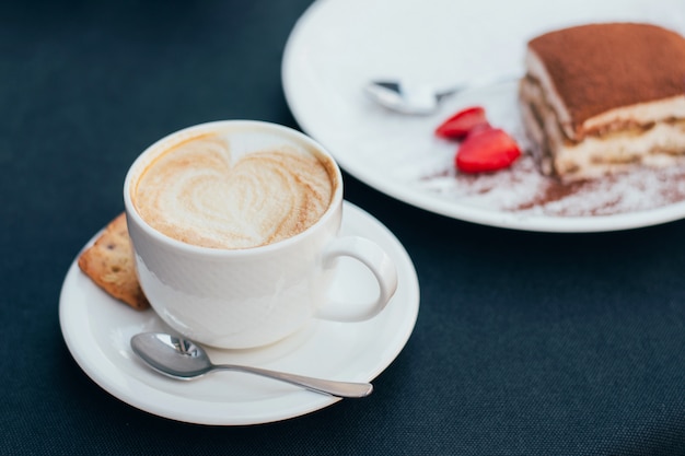 tazze di caffè e tiramisù sul tavolo nero con bella latte art a forma di cuore.