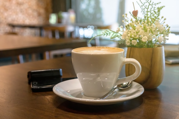 Tazze di caffè sul tavolo con finto decorano fiori finti e telefono cellulare