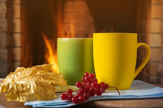 Tazze di tè o caffè e foglie d'autunno davanti al caminetto in una casa di campagna