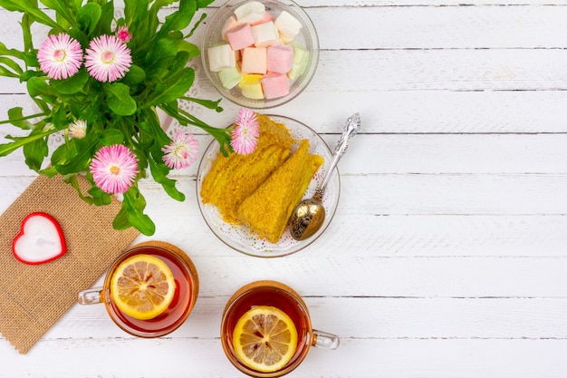 tazze di tè, pezzi di torta, bouquet di fiori rosa, marshmallow e candela a forma di cuore