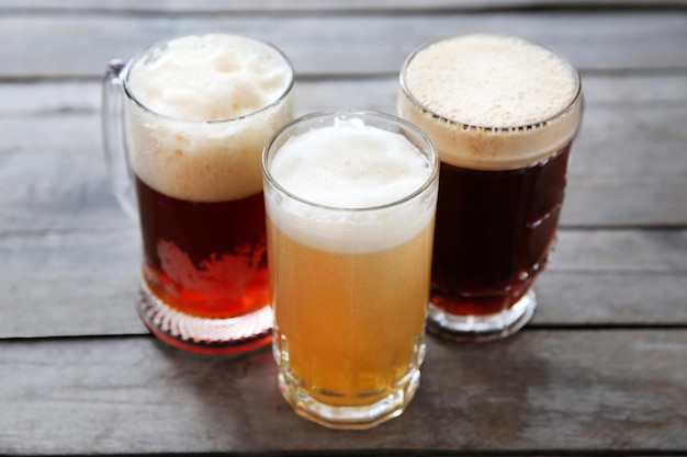 Tazze di vetro con diversi tipi di birra artigianale su tavola di legno