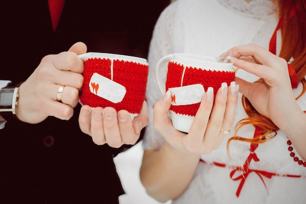 Tazze in copertine rosse lavorate a maglia con cuori con tè caldo e vapore nelle mani degli innamorati