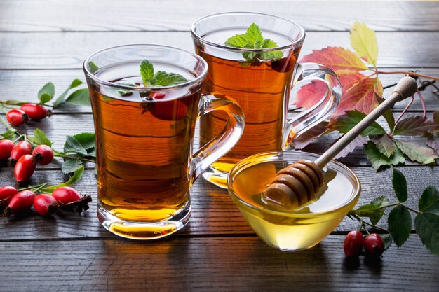 Tè al cinorrodonte in tazza trasparente con miele e frutti di bosco freschi. Bevanda di vitamina C sul tavolo scuro