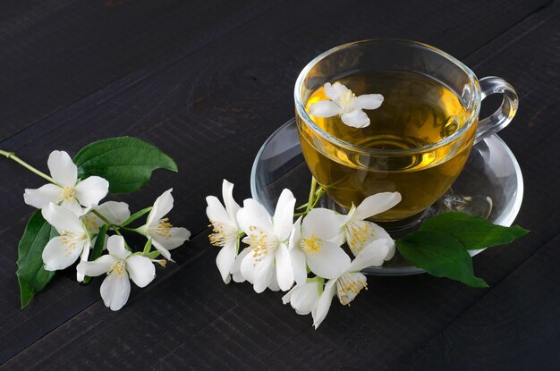 Tè al gelsomino con fiori di gelsomino su fondo di legno scuro.