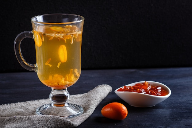 Tè al gelsomino con kumquat in una tazza di vetro su una tavola di legno sul nero