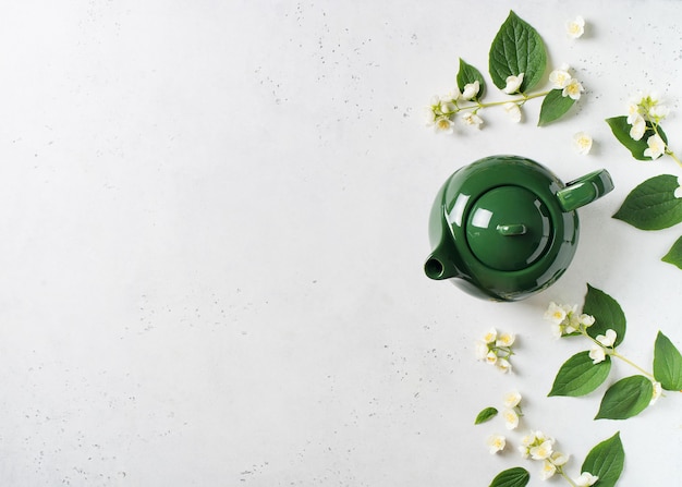 Tè al gelsomino con teiera, fiori e foglie su sfondo bianco, copia spazio, vista dall'alto