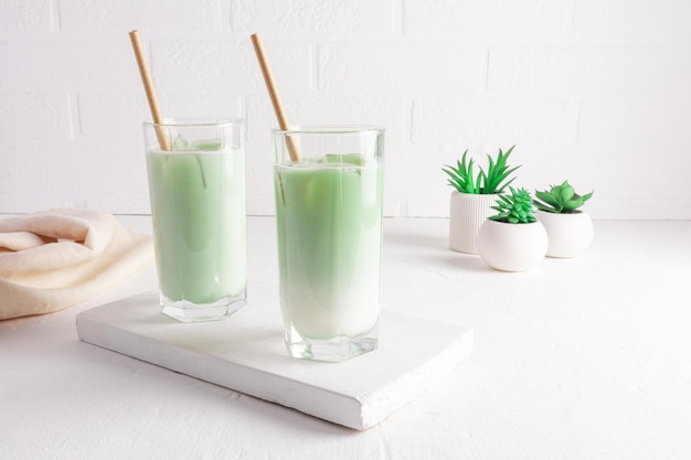 Tè al latte Matcha in bicchieri alti con paglia su una tavola di legno bianca una bevanda salutare purificazione del corpo miglioramento del metabolismo