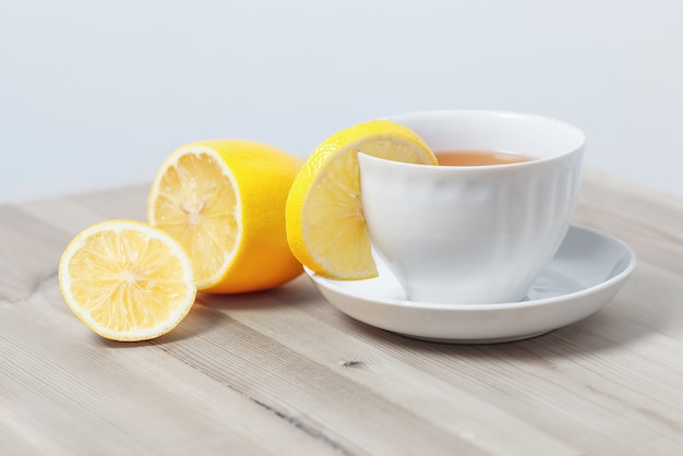 Tè al limone in una tazza bianca su un piattino su una superficie di legno