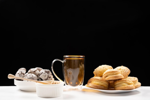 Tè al miele con biscotti al cacao e torte con ripieno cremoso su fondo nero
