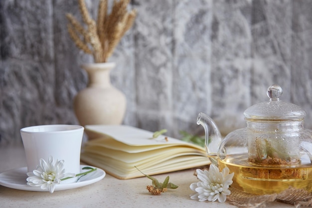 Tè al tiglio biologico in teiera con tazza di tè Crisantemi di grano decorazioni autunnali e taccuino Accogliente relax d'atmosfera a casa