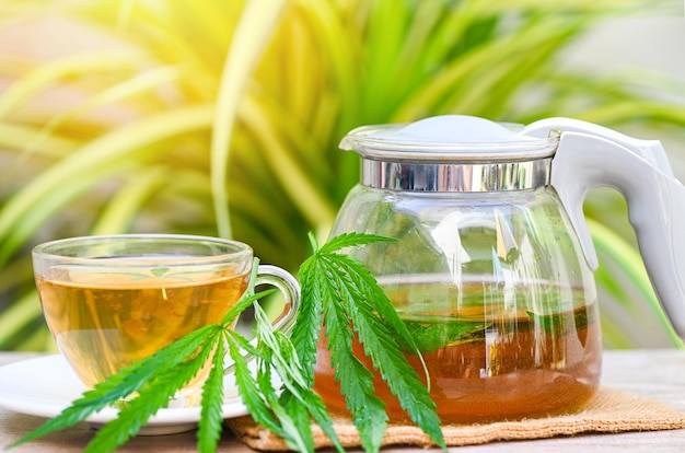 Tè alla cannabis alle erbe su tazza da tè con foglia di cannabis foglie di marijuana erba su sfondo verde natura, tè salutare con pianta di foglie di canapa THC CBD erbe cibo e concetto medico