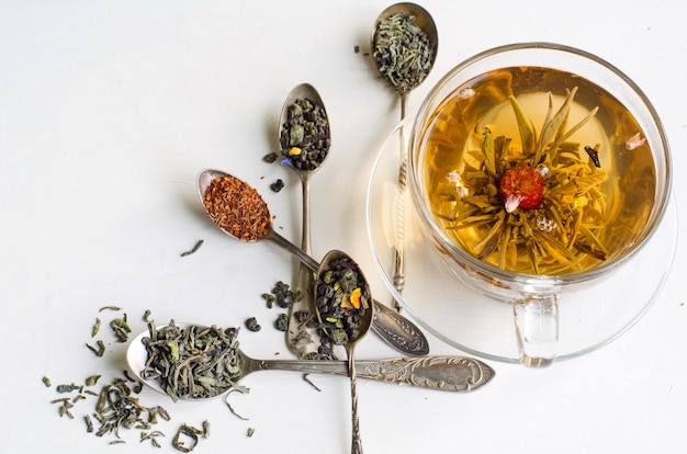 tè alla fioritura in una tazza di vetro e cucchiai d&#39;argento con vari tipi di tè