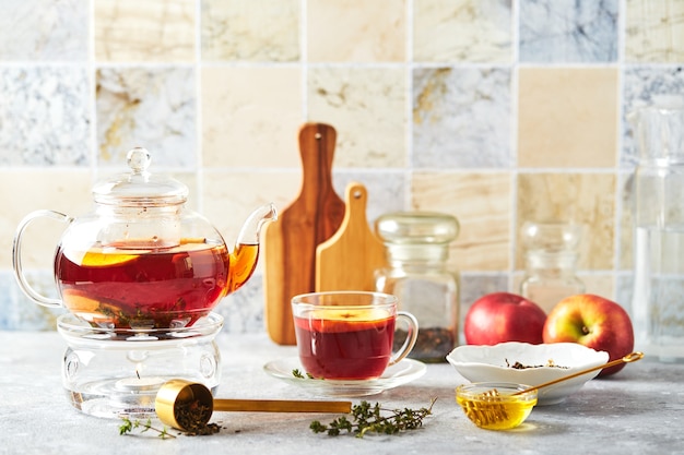 Tè alla frutta con mele e timo in teiera di vetro e tazza sul tavolo della cucina