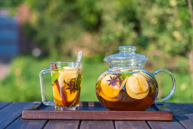 Tè alla mela sano in una teiera di vetro e una tazza nel giardino estivo su un tavolo di legno. Avvicinamento