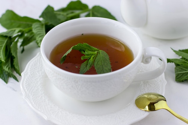 Tè alla menta in una tazza bianca e una teiera bianca su uno sfondo di marmo bianco Tè del mattino