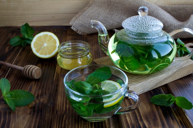 Tè alla menta nella tazza di vetro e teiera sul tavolo in legno rustico. Bevanda salutare. Avvicinamento.