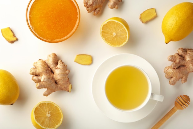 Tè allo zenzero con limone e miele su sfondo bianco.