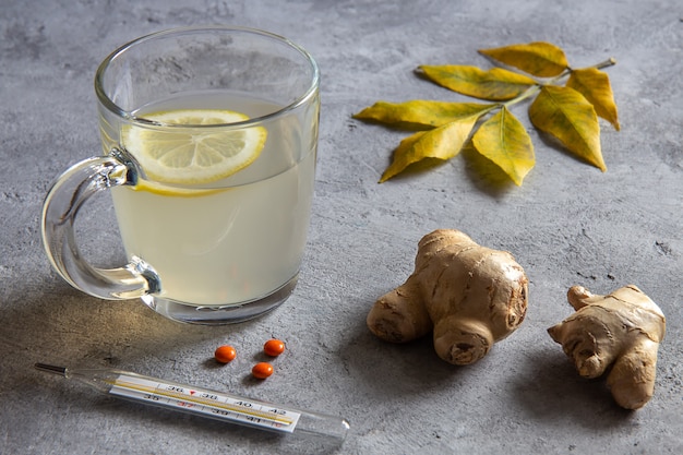 Tè allo zenzero con limone, radice di zenzero, termometro e foglie su un grigio