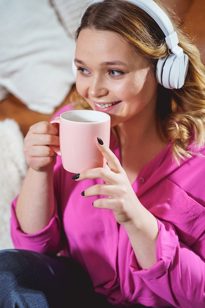 Tè aromatico. Allegra donna bruna che mantiene il sorriso sul viso, ascoltando musica in cuffia