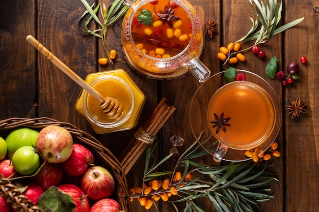 Tè autunnale con frutti di bosco e miele. Olivello spinoso e lamponi in una teiera di vetro, tazze con versato