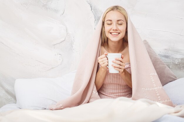 Tè bevente della donna attraente che si siede sul suo letto