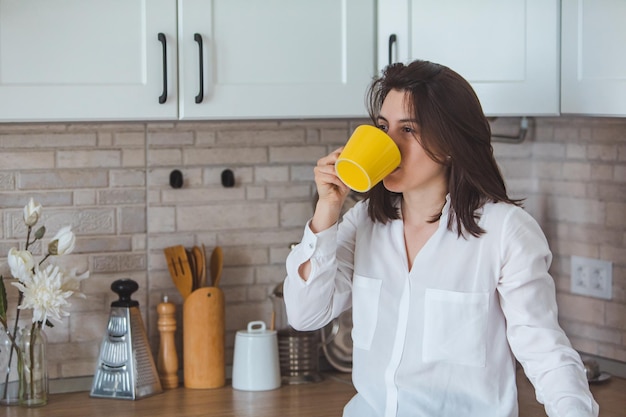 Tè bevente della giovane donna graziosa dalla tazza gialla alla cucina