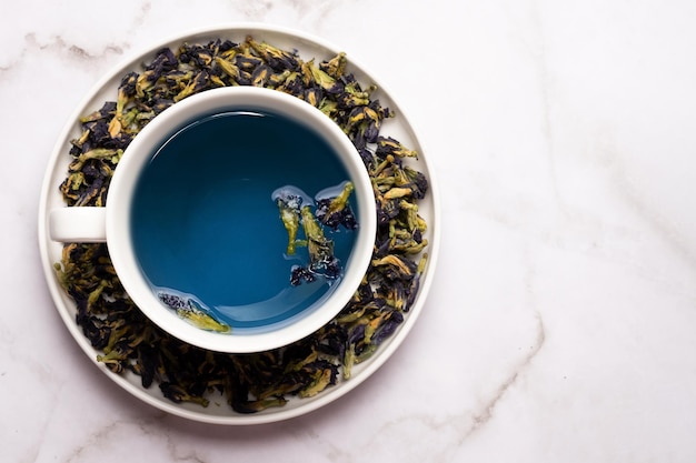 Tè blu alle erbe salutare, tazza bianca con anchan dal fiore di pisello farfalla su fondo di marmo.