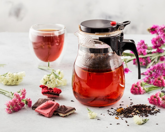 Tè caldo alla frutta rossa in una teiera di vetro su sfondo chiaro decorato con fiori