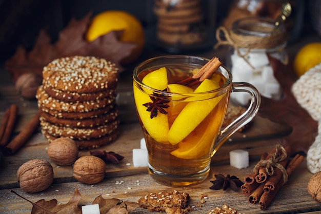 Tè caldo autunnale con limone e spezie in tazza di vetro. Tè sano con biscotti, noci e foglie intorno. Concetto di autunno